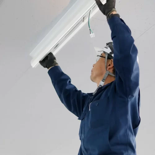 An electrician installing a fluorescent light to a ceiling